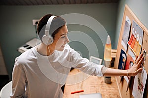 Young white woman in headphones smiling and looking at pin board