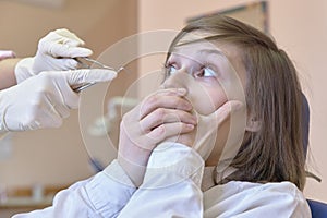 A young white woman in horror looks at the dentist`s hands and tools in her hands.