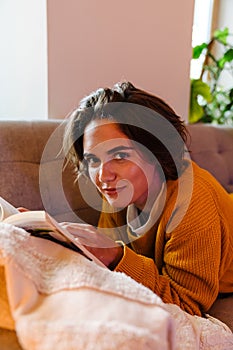Young white woman reading book while lying on couch