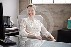 Young white woman sitting at office desk smiling to camera