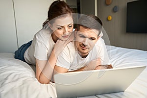 Young wife looks into laptop over shoulder of her husband