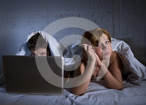 young wife upset unsatisfied and frustrated in bed while husband work on computer laptop ignoring her