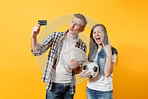 Young win couple, woman man, football fans holding bundle of dollars money, credit card, soccer ball, cheer up support