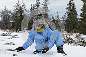 Young winter child experiencing making cold snowballs over mountain trees