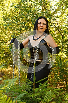 A young witch in black clothes with chains in the hands in the forest. Halloween.