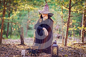 A young witch in a hat sits on a stump in the woods, her head propped up by her hand, sad