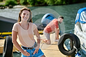 A young womaan standing on the dock while her man untying the boat