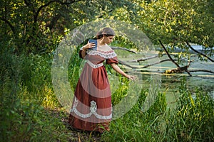 A young woman in a 19th century dress by the river. Girl with a book in his hand, summer day. The photo