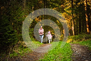 Young woman with 2 years old daughter together runs on country in forest. Cheerful female exercising outdoor with her child