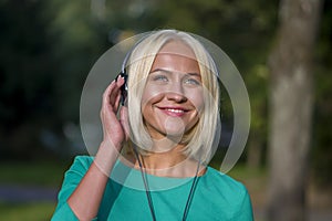 Young woman 25-30 years old in the Park listening to music with headphones, happy expression on her face,