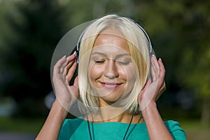 Young woman 25-30 years old in the Park listening to music with headphones, happy expression on her face,