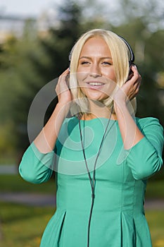 Young woman 25-30 years old in the Park listening to music with headphones, happy expression on her face,