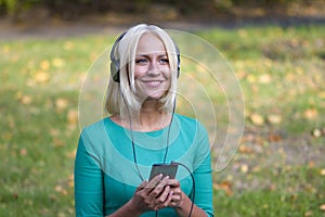 A young woman 25-30 years old in the Park listening to music with headphones from her phone,