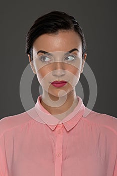 A young woman of 30-35 years old in a pink blouse on a gray background, restrained emotions. Maybe she works in an office