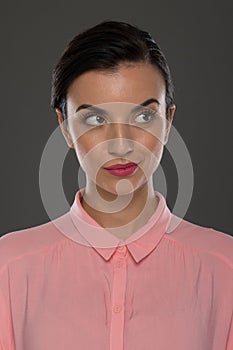 A young woman of 30-35 years old in a pink blouse on a gray background, restrained emotions. Maybe she works in an office