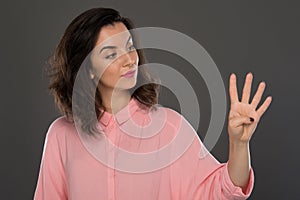 A young woman of 30-35 years old in a pink blouse on a gray background, restrained emotions. Maybe she works in an office