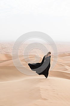 Young woman in Abaya posing in desert landscape.