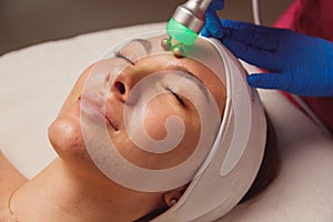 Young woman with acne getting ultrasound skin cleansing and face treatment at beauty salon