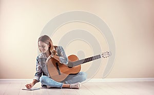 Young woman with acoustic guitar composing song near grey wall.