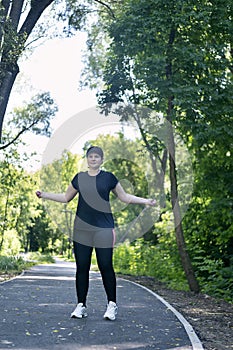 Young woman in activewear choosing healthy lifestyle. Plus size woman jumping rope in the park. Body positivity. Vertical frame