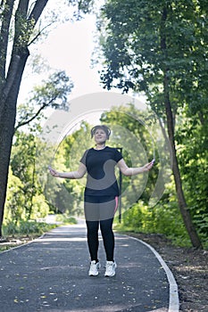 Young woman in activewear choosing healthy lifestyle. Plus size woman jumping rope in the park. Body positivity. Vertical frame