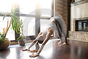 Young woman in adho mukha svanasana pose, home interior backgrou photo