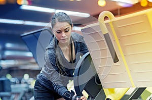 Young woman adjusting leg press machine in gym