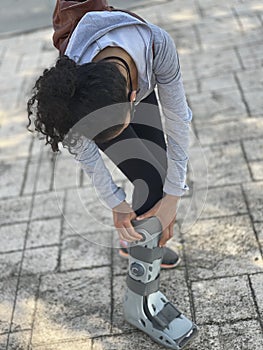 Young woman adjusting orthopedic boot used in rehabilitation for foot injury, fracture or ankle sprain. Patient walking down the