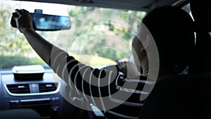 Young woman adjusting rear view mirror before driving. Safe driving concept.