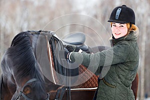 Young woman adjusting stirrups before riding horse photo