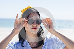 A young woman adjusts her sunglasses at the beach, unaltered