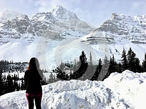 A young woman admiring an incredible view of a dark green forest in the foreground and snow covered mountains peaks