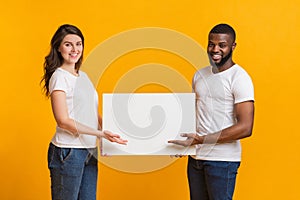 Young woman and afro man holding and pointing at blank placard