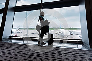Young woman in the airport, looking through the window at planes.