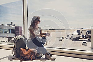 Young woman in the airport, looking through the window at planes and drinking coffee, travel, vacations and active lifestyle conce