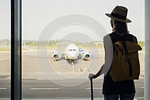 Young woman in the airport looking through the window at planes, travel, tourism, transportation, vacations and active lifestyle c