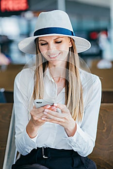 Young woman in the airport, using smartphone and drinking coffee, travel, vacations and active lifestyle concept