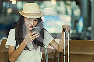Young woman in airport waiting for air travel using smart phone.