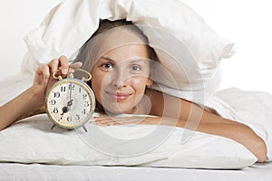 Young woman with alarmclock on the bed at morning