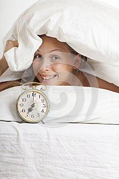 Young woman with alarmclock on the bed at morning