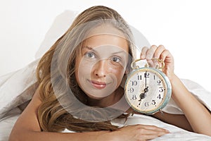 Young woman with alarmclock on the bed at morning