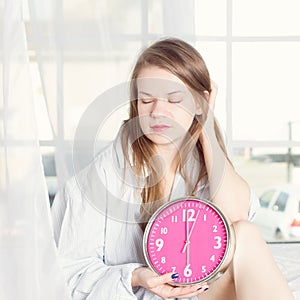 Young woman with alarmclock on the bed at morning