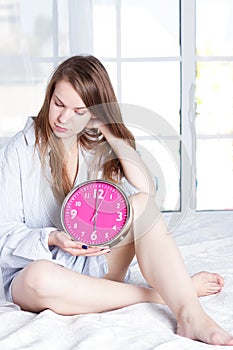 Young woman with alarmclock on the bed at morning