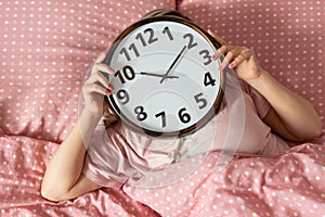 Young woman with alarmclock on the bed at the morning. Waking up on an alarm clock. Good morning. Healthy sleep. The