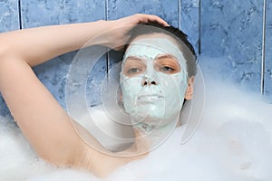 Young woman with alginate mask relaxing lying in bathroom with foam at home.