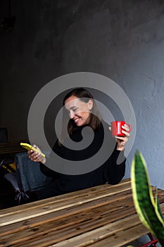 Young woman alone drinking in cafe on the terrace with a smartphone in her hands