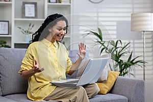 Young woman alone at home happily talking alone using laptop for video call, Hispanic woman sitting at home in living