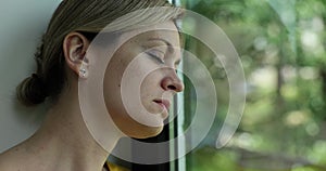 Young woman alone at home thinks about loneliness or grief and sits window and looks out into street with lonely