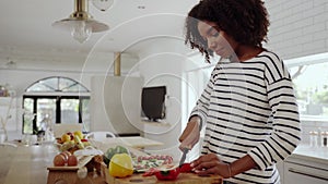 Young woman alone in the modern kitchen cutting red bell pepper with a knife on chopping board