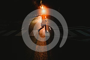 Young woman alone walking and crossing a lonely street by a pedestrian crossing at sunset